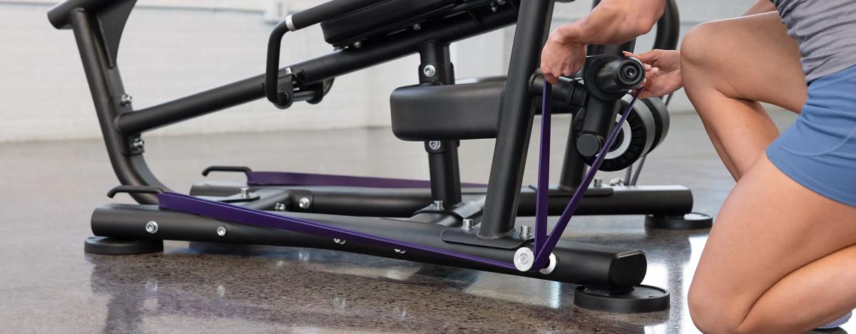A person placing a purple resistant band on the pegs at the bottom of the machine.