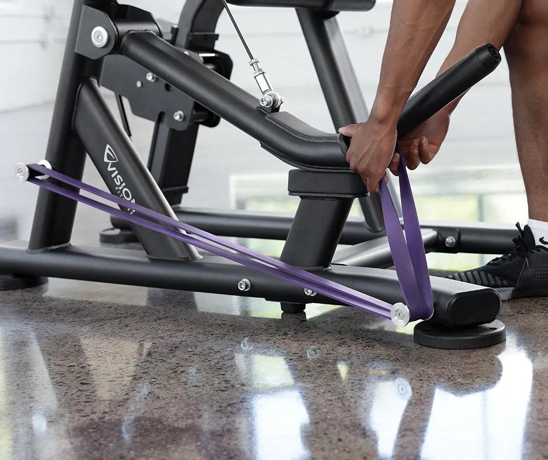 A person placing a purple resistant band on the pegs at the bottom half of the machine.