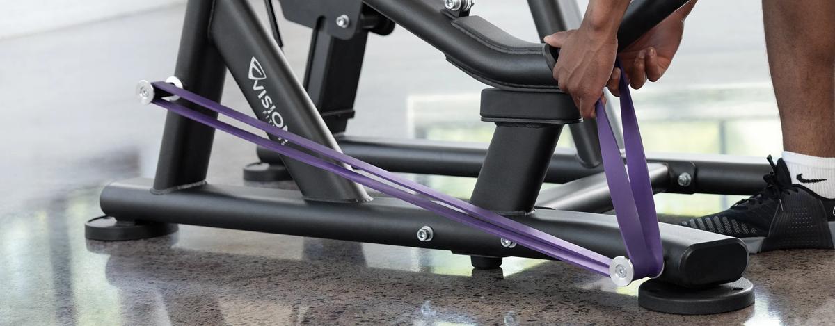 A person placing a purple resistant band on the pegs at the bottom half of the machine.