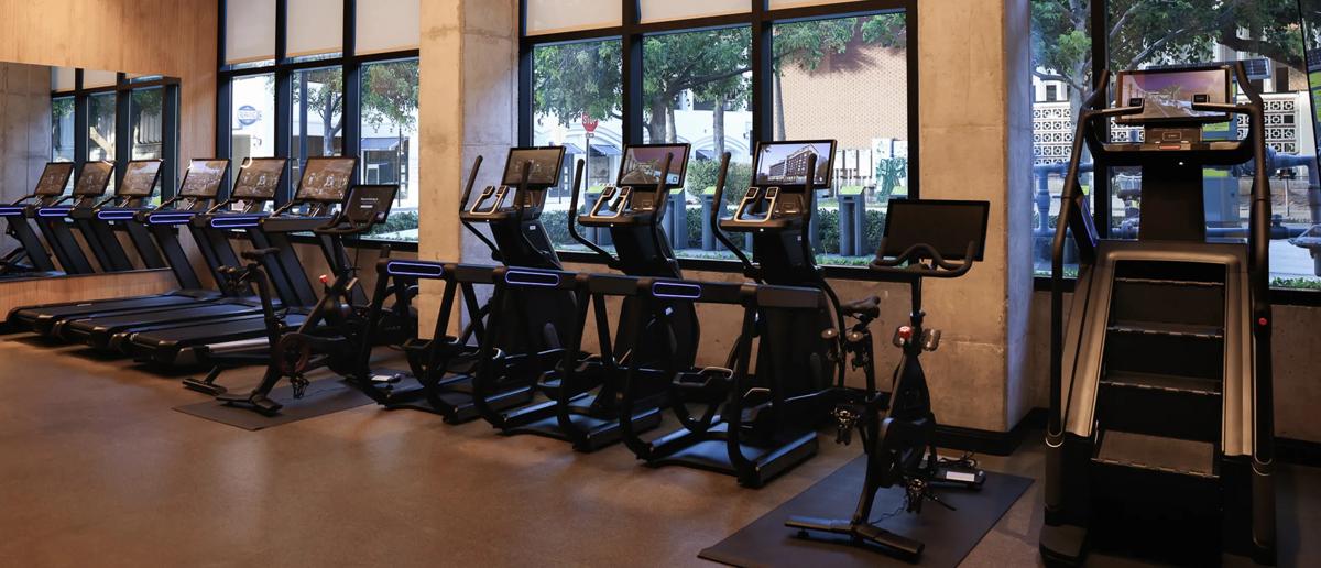 Matzwarte Matrix Fitness Onyx-cardio- en krachtapparatuur vult een modern fitnesscentrum met geïntegreerde schermen, blauwe accentverlichting, spiegelwanden en een ruim, hoogwaardig ontwerp.