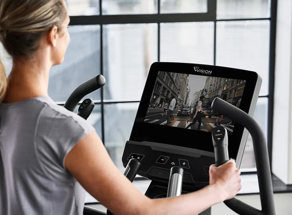 A person in a grey workout shirt working out on a Vision elliptical watching live tv on the entertainment console.