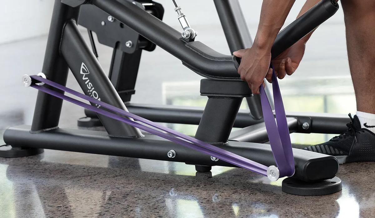 A person placing a purple resistant band on the pegs at the bottom half of the machine.
