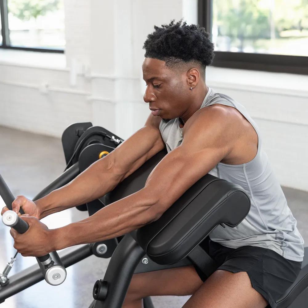 Een persoon in een grijs trainingsshirt die shoulder press gebruikt met gestrekte linkerarm.