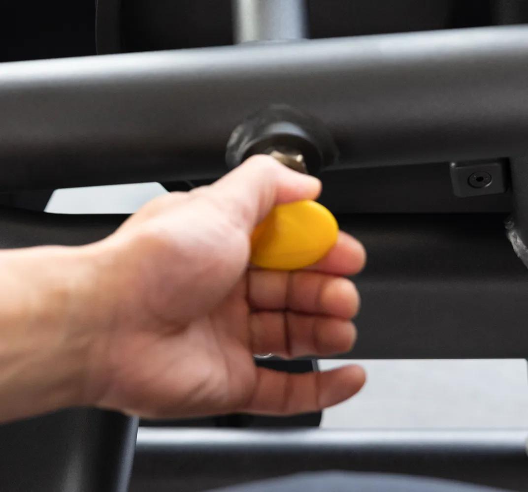 Close-up of a person using the Keystone Seated Leg Curl adjustment arm with yellow pop-pins.