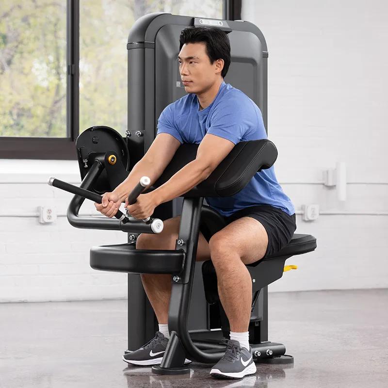 Person in the starting position on the Keystone Biceps Curl machine, seated with arms extended and hands gripping the rotating handles.