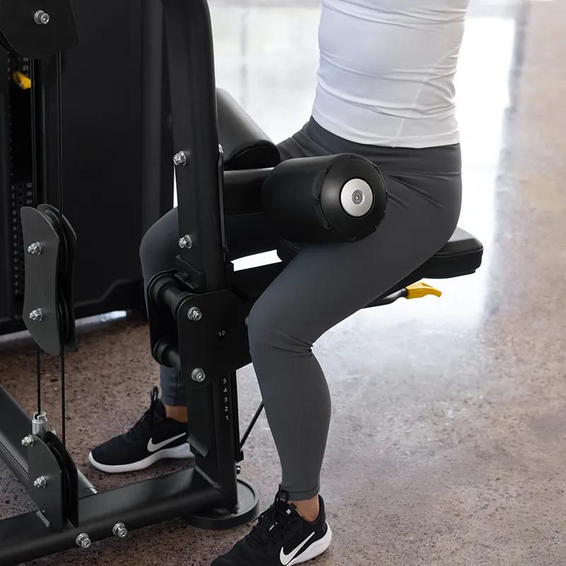 Close-up of a person seated on the Vision Fitness Lat Pulldown machine in Matte Black, with her legs secured under the padded thigh rollers and the yellow adjustment lever visible below the seat.