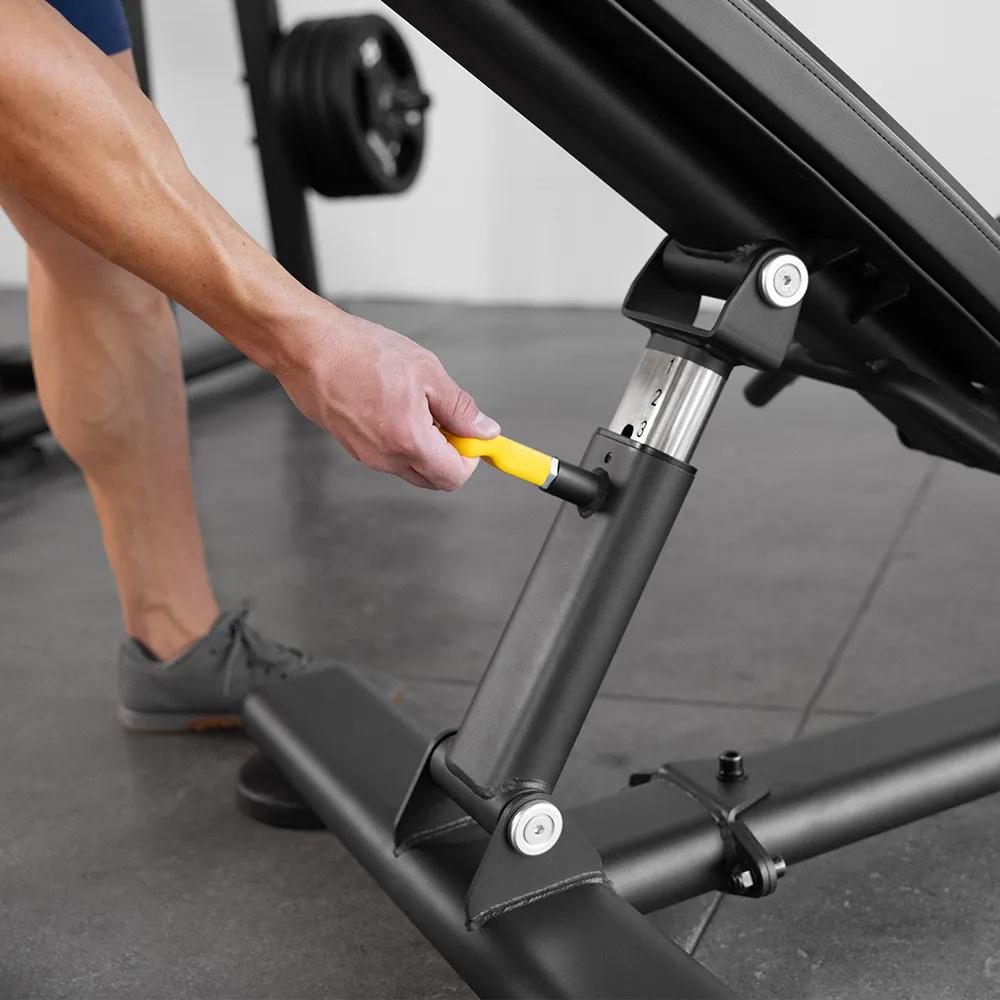 A person pulling yellow adjustment handle on the back side of a workout bench.