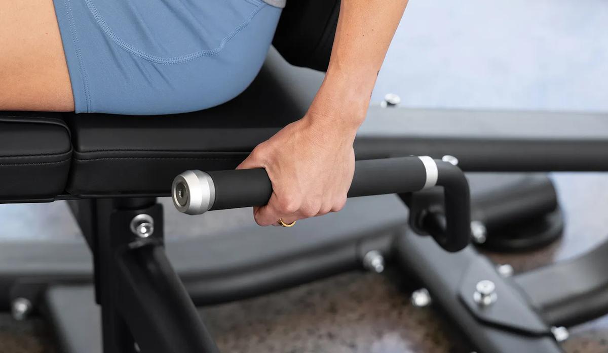 A person's left hand on the rubber handles on the side of the Vision Leg Extension.