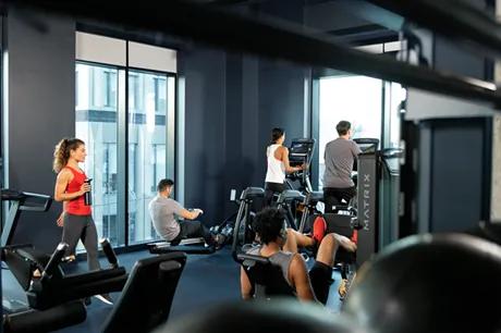 A group of people working out in a bright gym on cardio and strength equipment