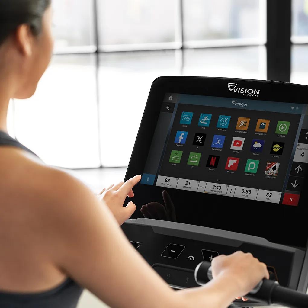 Two people exercising on Vision Fitness stationary bikes with interactive screens in a bright, modern gym.