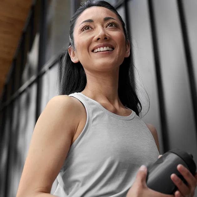A woman smiling and looking off into the distance while holding a water bottle.