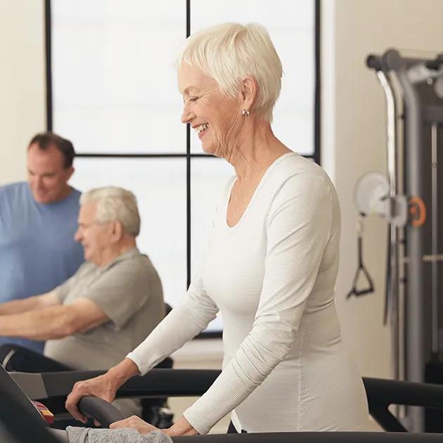 An older woman walking on a Matrix treadmill while smiling.