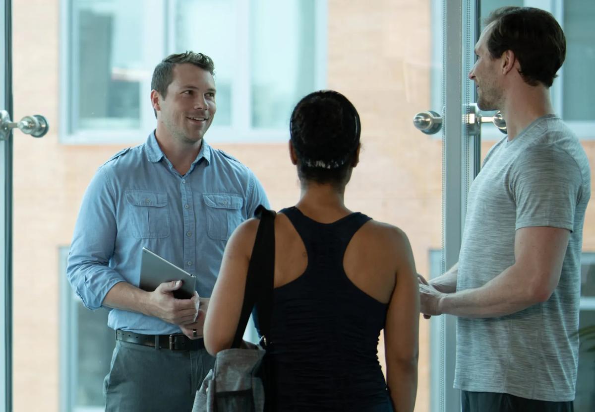 A person in business casual clothing, speaking with two people in workout clothes