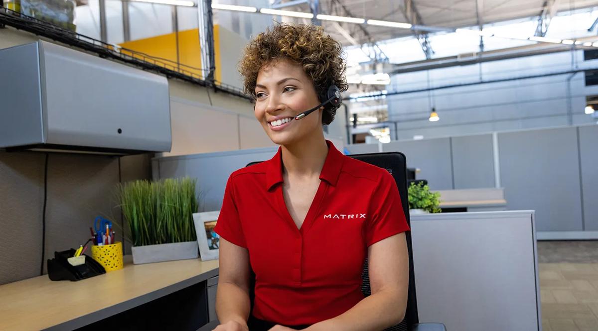 Woman smiling and sitting at a desk with a headset on in an office
