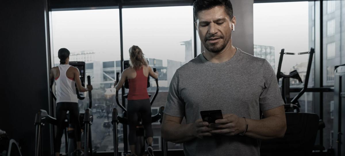 Una persona con un auricolare all'orecchio sinistro e il cellulare in mano, si allena sulle elliptical Matrix insieme a due altre persone.