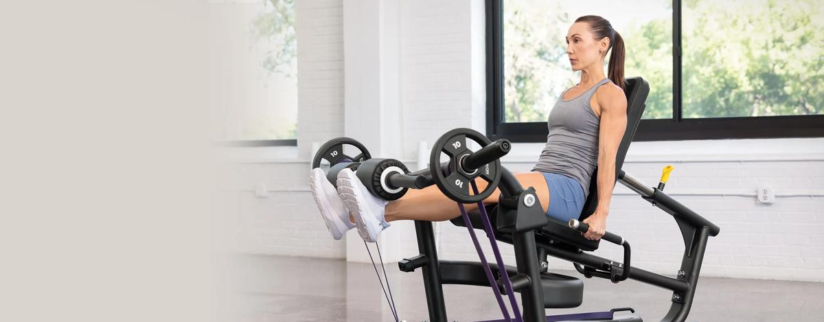 A person with their legs straight out with weights and resistant bands on the Vision Leg Extension.