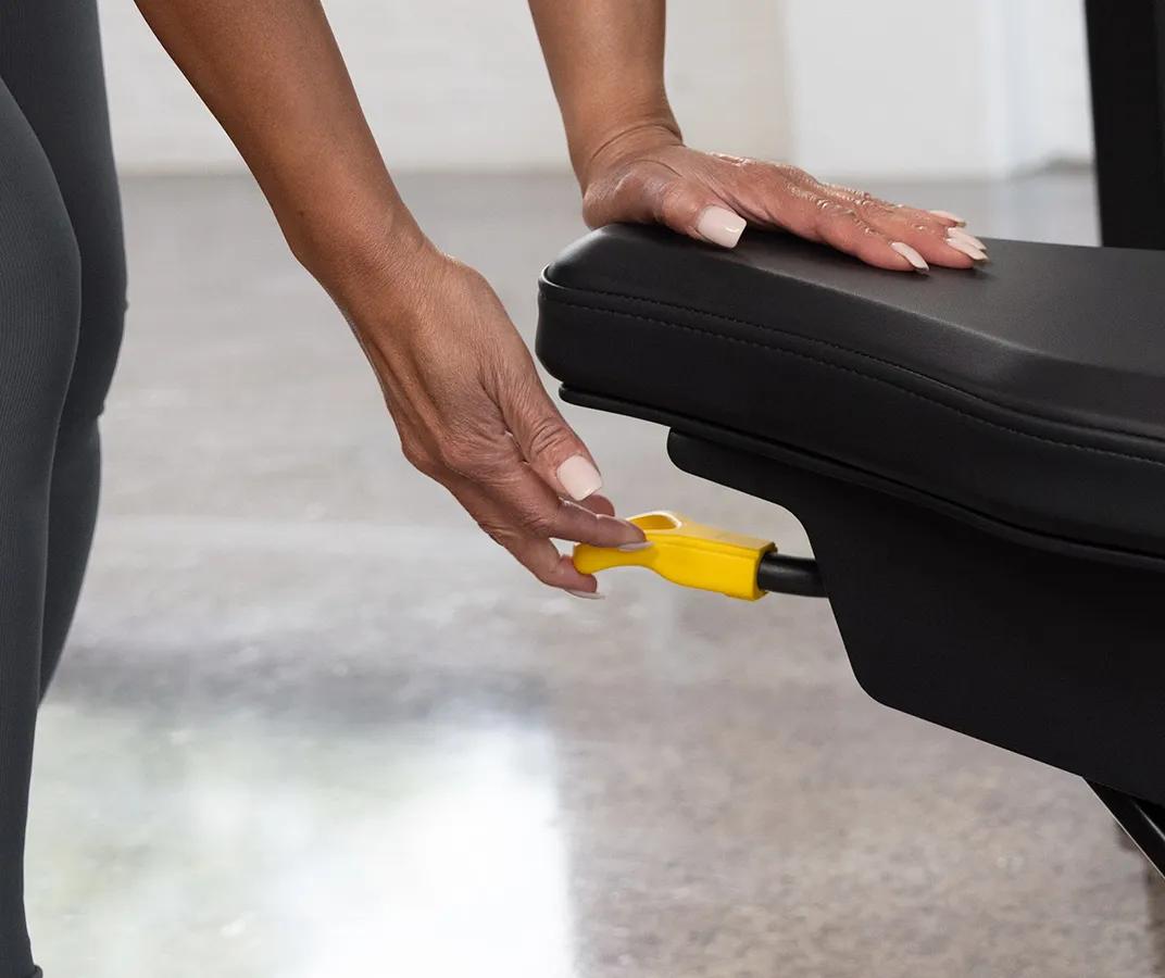 Close-up of a person adjusting the seat height on the Vision Fitness Shoulder Press machine in Matte Black using the yellow lever beneath the seat.