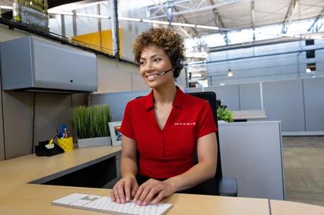 A person in a red Matrix shirt with a headset on smiling typing on a keyboard