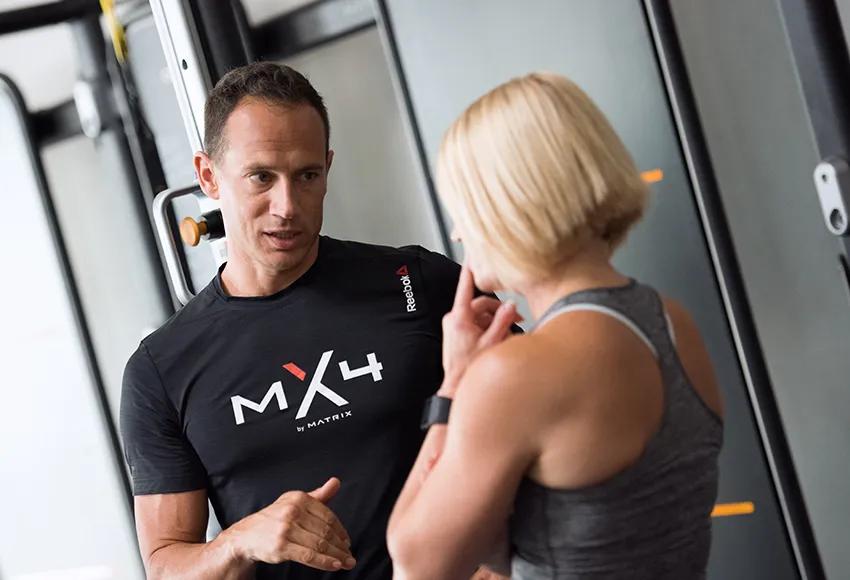 A person in a grey tank talking to another person in a black MX4 t-shrit