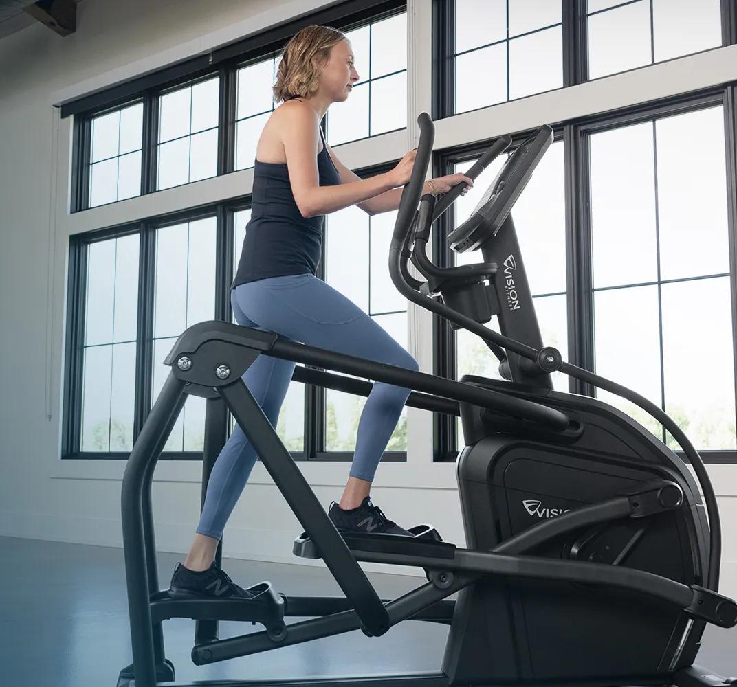 Side view of a person using the Summit Ascent Trainer in a large, open room.