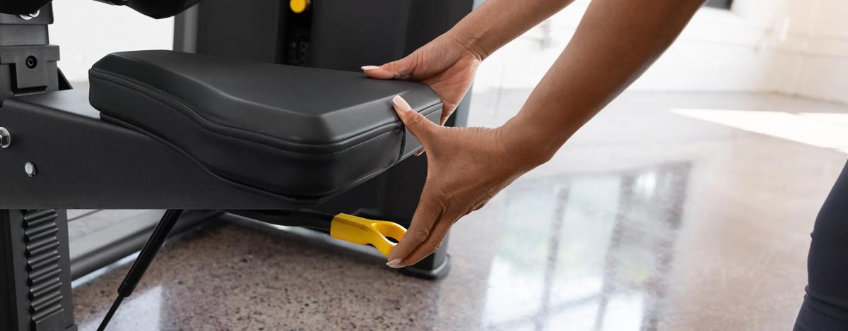 Close-up of a person adjusting the seat height on the Vision Fitness Lat Pulldown machine in Matte Black using the yellow lever below the seat.