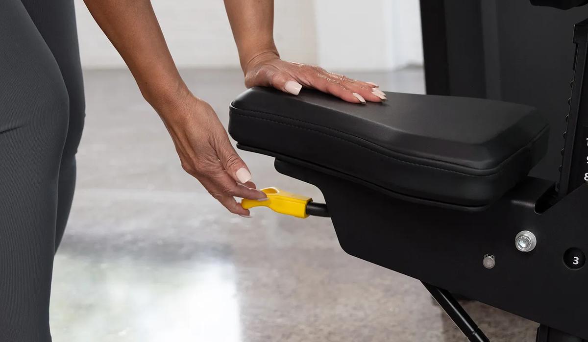 Close-up of a person adjusting the seat height on the Vision Fitness Shoulder Press machine in Matte Black using the yellow lever beneath the seat.