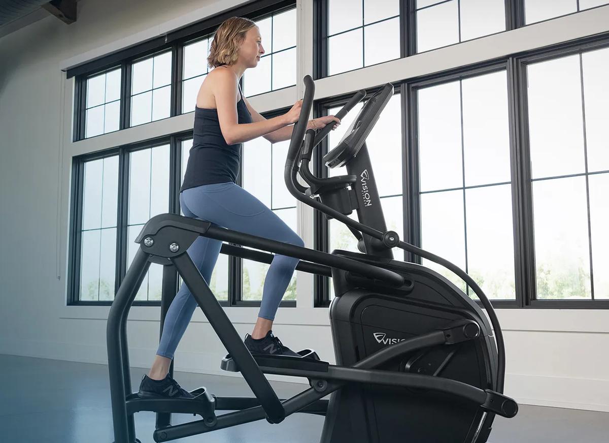 Side view of a person using the Summit Ascent Trainer in a large, open room.